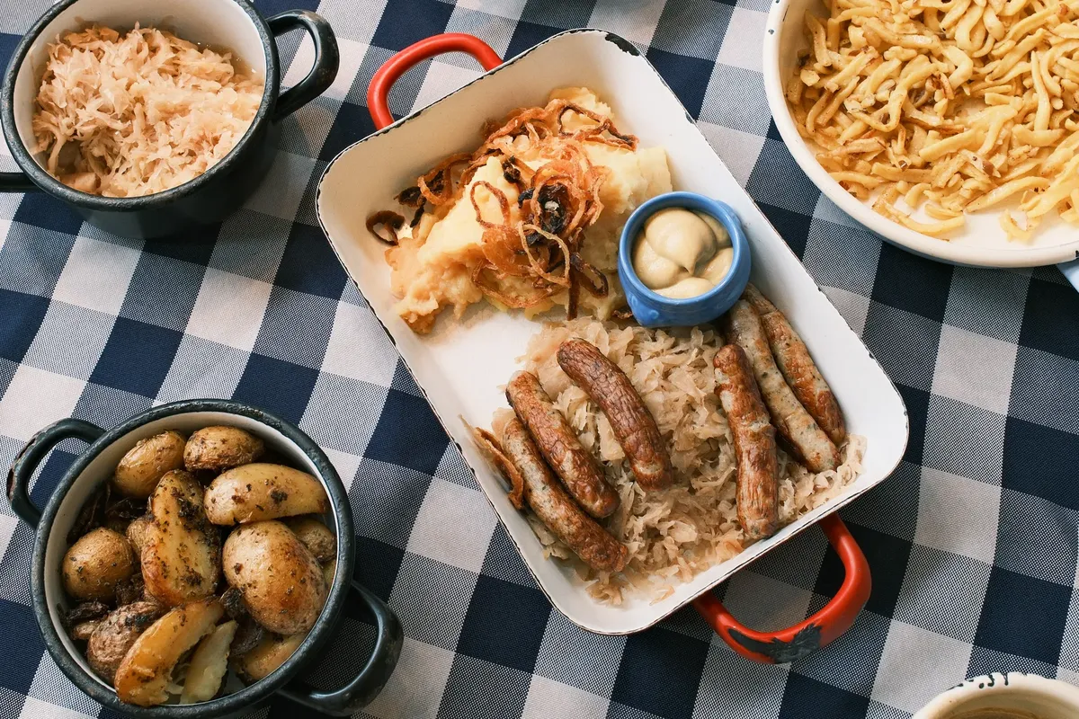 德國盛宴，包含香腸、泡菜、土豆與意麵，擺放在條紋桌布上