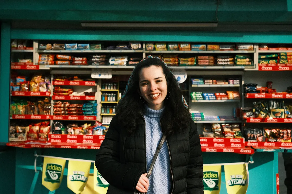 A cheerful woman in a black jacket smiling in front of a colorful store display.